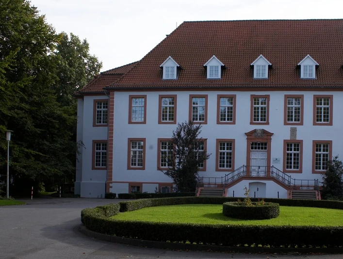 Ein gepflegtes Herrenhaus mit weißer Fassade, vielen Fenstern und einem dekorativen Garten.