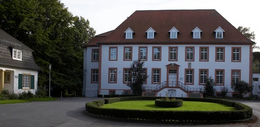 Reckenberg in Wiedenbrück Ein gepflegtes Herrenhaus mit weißer Fassade, vielen Fenstern und einem dekorativen Garten.