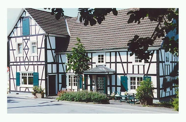 Kunsthaus Zur Mitte Fachwerkhaus mit weiß getünchten Fassaden und dunklem Holz, grünen Fenstern im ländlichen Ambiente.