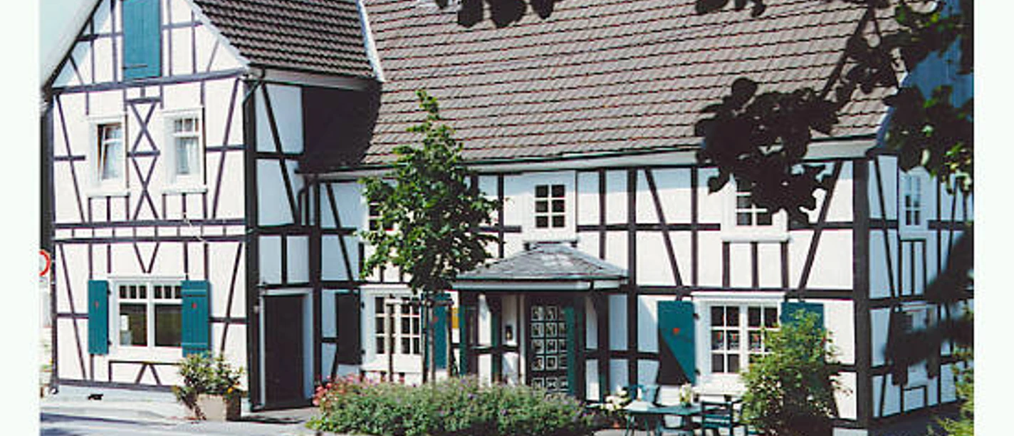 Kunsthaus Zur Mitte Fachwerkhaus mit weiß getünchten Fassaden und dunklem Holz, grünen Fenstern im ländlichen Ambiente.