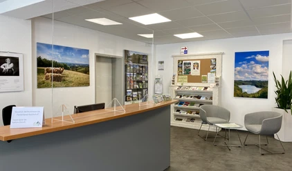 Kur- und Touristinfo Reichshof Empfangsbereich mit Informationsbroschüren, modernen Möbeln, Landschaftsfotos und einem Begrüßungsschild.