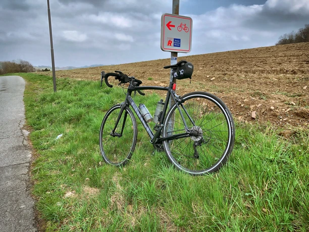 Schwalbe Fahrradpark Rennrad lehnt an einem Schild auf grünem Gras neben einem gepflügten Feld und einer Straße.