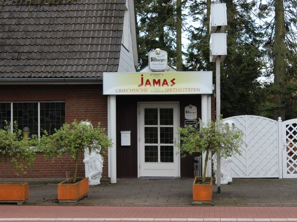 Jamas Eingang eines griechischen Restaurants mit rotem Vordach, Blumenkästen und Ziegelsteinfassade.