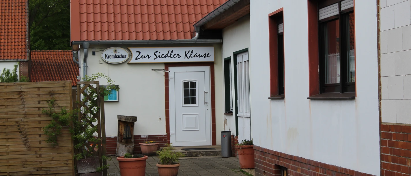 Zur Siedlerklause, een traditionele herberg met een rood pannendak, witte muren en bloempotten.