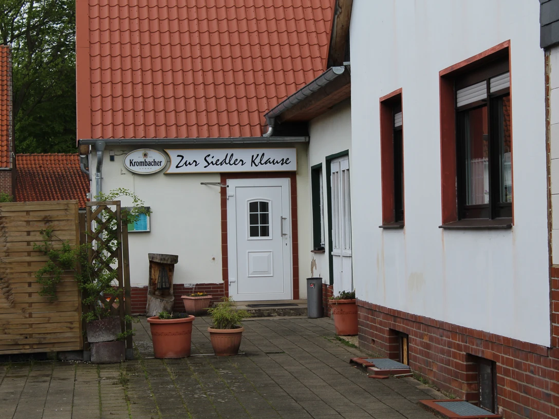 Zur Siedlerklause Zur Siedlerklause, ein traditionelles Gasthaus mit rotem Ziegeldach und weißen Wänden sowie Blumenkübeln.