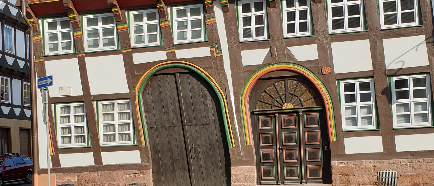 Fass 5 des Bierpfads: Infopunkt vor einem schiefen Fachwerkhaus mit großen, bunten Torbögen.