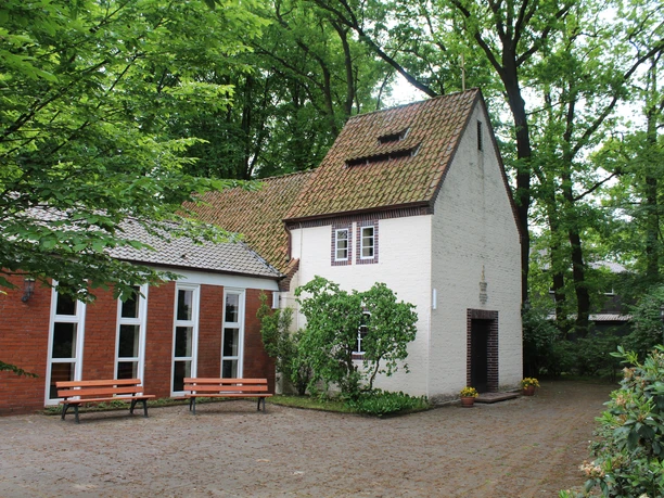 Historische Kapelle inmitten grüner Bäume. Ziegelbau mit Satteldach und einladendem Vorgarten.