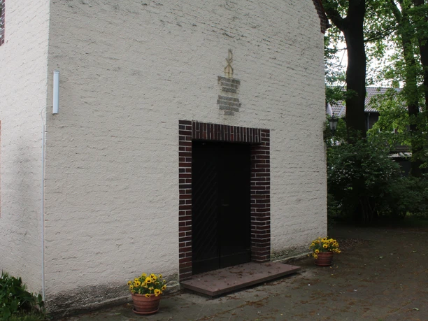 Kapelle Nordel Eingang der Kapelle Nordel mit dunkelbrauner Tür, gerahmt von blühenden Pflanzen in Töpfen.