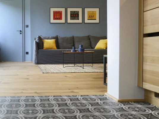 Appartement No 16 Modernes Appartement mit grauem Sofa, gelben Kissen, stilvollen Bildern und gemustertem Boden.