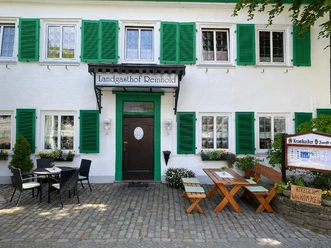 Draußen_1.jpg Fassade eines traditionellen Gasthauses mit grünen Fensterläden, Holzbänken und Pflanzendekoration.