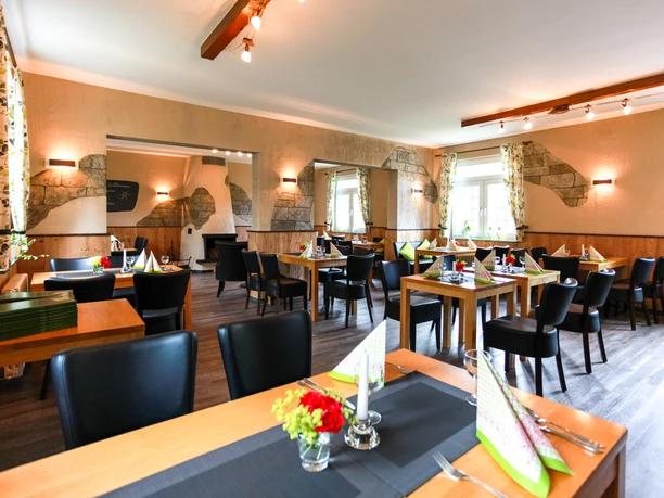 Frühstückszimmer (1).jpg Ein gemütlicher Gastraum mit Holz- und Steinelementen, gedeckten Tischen und blühenden Tischdekorationen.