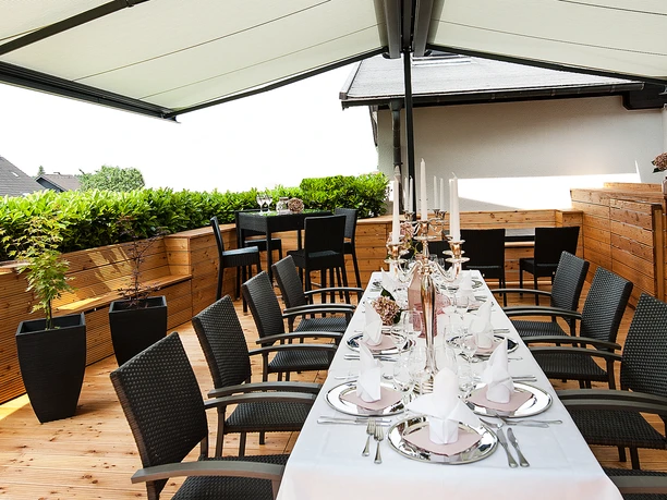 4599 panorama.jpg Sonnengeschützter Balkon mit elegant gedecktem Tisch, modernen Stühlen und grüner Heckenbepflanzung.