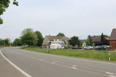Rasthaus Wietersheim Ein Rasthaus neben einer Landstraße, umgeben von Bäumen und geparkten Autos am Straßenrand.