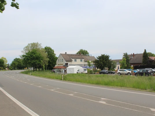 Rasthaus Wietersheim Ein Rasthaus neben einer Landstraße, umgeben von Bäumen und geparkten Autos am Straßenrand.