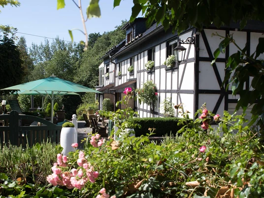 Restaurant Heidestübchen Fachwerkhaus mit blühendem Garten, grünem Sonnenschirm und Naturumgebung an einem sonnigen Tag.