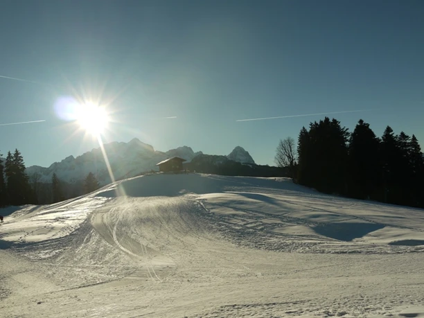 Eckbauer im Winter Verschneiter Hang mit kleiner Hütte vor Bergkulisse im Gegenlicht der tief stehenden Sonne