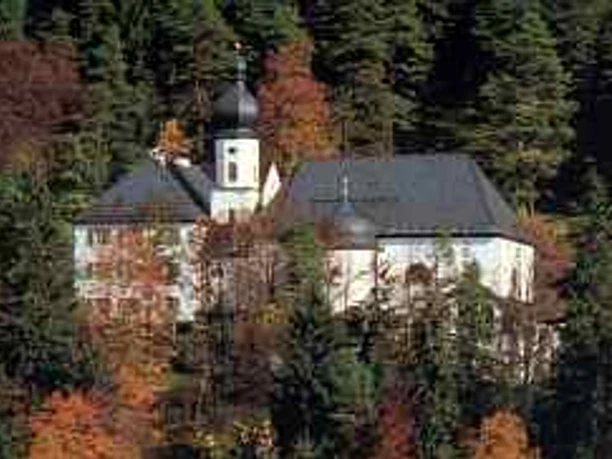 St. Anton Weißes Kirchengebäude mit Zwiebelturm, umgeben von herbstlichem Waldbestand