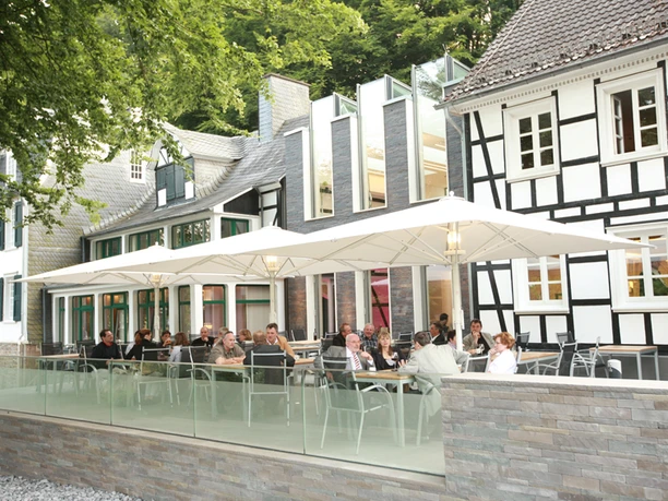 Seminar- und Tagungshotel Große Ledder mit Außenterrasse Eine Terrasse mit Gästen vor modernen und traditionellen Fachwerkgebäuden, umgeben von Bäumen.