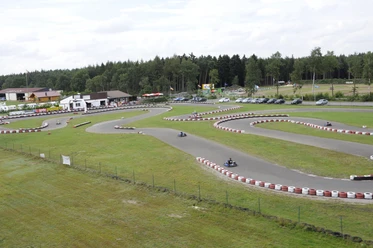 Emslandring Go-Kart-Bahn mit geschwungenem Asphaltkurs, mehreren Fahrern und Gebäuden im Hintergrund.
