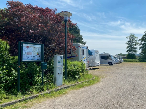 Wohnmobilstellplatz Rehburg Wohnmobilstellplatz mit mehreren Fahrzeugen neben grünen Büschen und einer Informationstafel unter blauem Himmel.