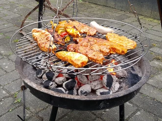 Symbolbild: Grillen Grill voller Fleisch und Gemüse auf Holzkohle, dazwischen glimmende Kohlen.