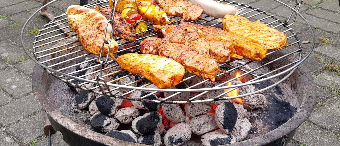 Symbolbild: Grillen Grill voller Fleisch und Gemüse auf Holzkohle, dazwischen glimmende Kohlen.