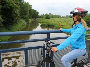 Eyterbrücke Thedinghausen Eine Radfahrerin blickt von einer Brücke über einen von Bäumen gesäumten Fluss in Thedinghausen.