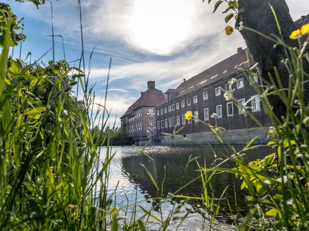 Schloss Oberwerries, Hamm Historisches Gebäude spiegelt sich pittoresk im Wasser, umrahmt von grüner Natur.