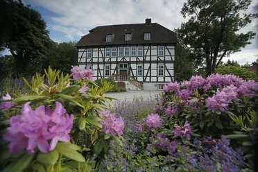 Fachwerkhaus umgeben von blühenden Rhododendren und Lavendel, an einem klaren Frühlingstag fotografiert.