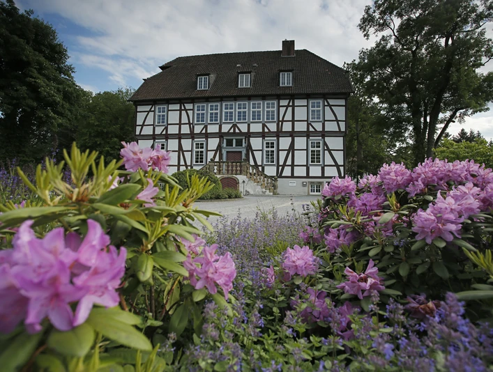 Fachwerkhaus umgeben von blühenden Rhododendren und Lavendel, an einem klaren Frühlingstag fotografiert.