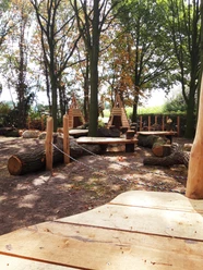 Holzspielplatz im Wald mit großen Baumstämmen, Seilen zum Balancieren und hölzernen Schutzhütten.