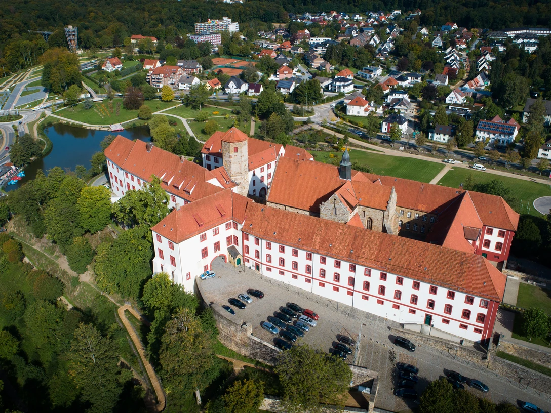 Schloss Iburg aus der Vogelperspektive Luftaufnahme eines historischen Schlosses mit rotem Dach, umgeben von Wohnhäusern und Grünflächen.Aerial view of a historic castle with a red roof, surrounded by residential buildings and green spaces.Luftfoto af et historisk slot med rødt tag, omgivet af beboelsesejendomme og grønne områder.Luchtfoto van een historisch kasteel met een rood dak, omringd door woongebouwen en groene ruimtes.