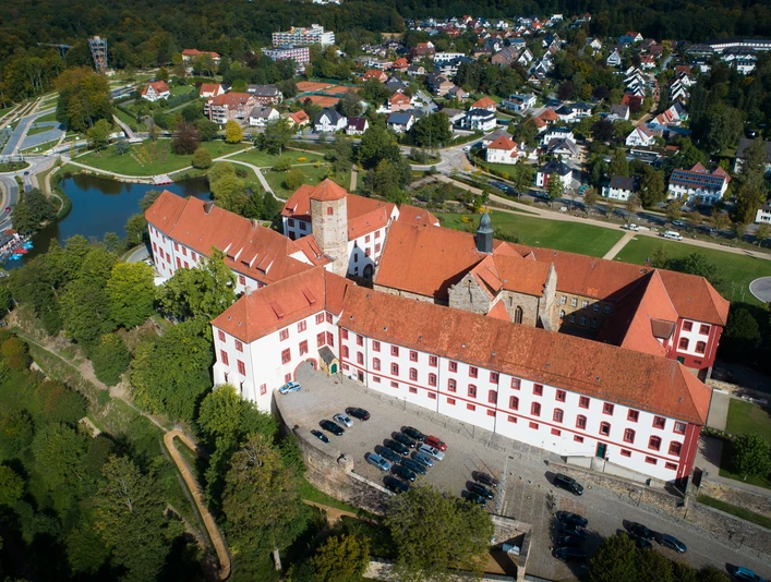 Schloss Iburg aus der Vogelperspektive Luftaufnahme eines historischen Schlosses mit rotem Dach, umgeben von Wohnhäusern und Grünflächen.Aerial view of a historic castle with a red roof, surrounded by residential buildings and green spaces.Luftfoto af et historisk slot med rødt tag, omgivet af beboelsesejendomme og grønne områder.Luchtfoto van een historisch kasteel met een rood dak, omringd door woongebouwen en groene ruimtes.