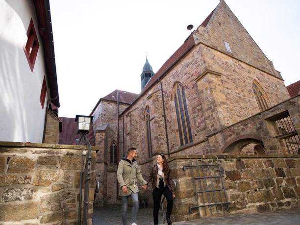 Mittelalter-Atmosphäre auf Schloss Iburg Couple walking in an old town alley, flanked by historic stone houses and a church in the background.