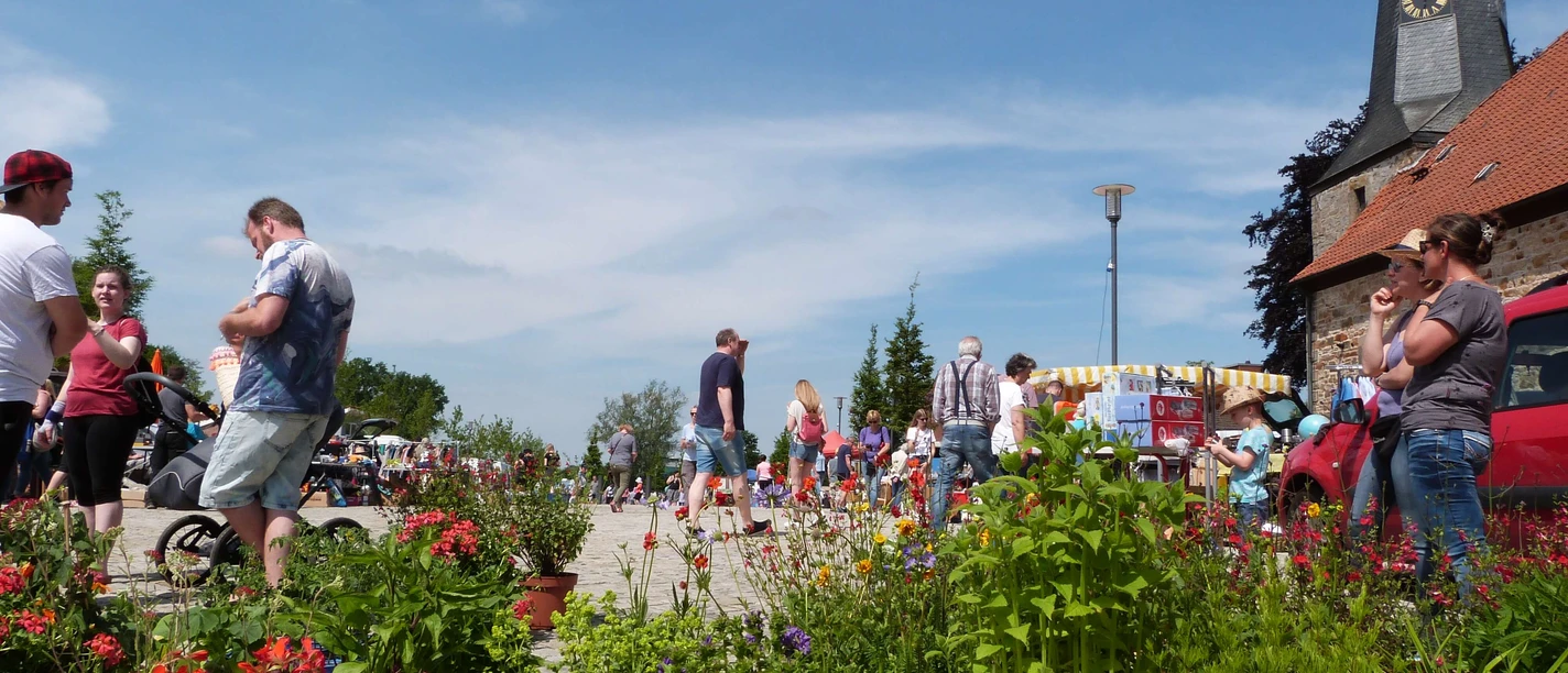 troedelmarkt-rehburg-pflanzen.JPG Menschen schlendern zwischen bunten Pflanzen und Verkaufsständen auf einem Freilufttrödelmarkt.