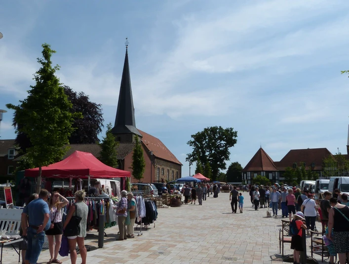 troedelmarkt-rehburg-stadtplatz-staende.JPG Ein Marktplatz mit Ständen, Menschen bummeln; im Hintergrund eine Kirche und Bäume sichtbar.