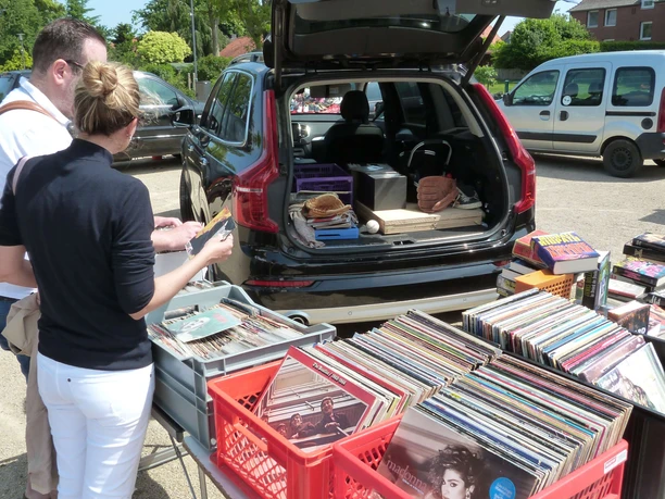 Zwei Personen stöbern an einem geöffneten Kofferraum voller Schallplatten bei einem Flohmarkt im Freien.