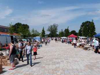 troedelmarkt-rehburg-platz.JPG Ein weitläufiger Flohmarkt auf einem gepflasterten Platz, umringt von Verkäufern unter bunten Zelten.