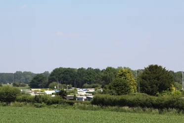 Campingplatz Coppel e.V. Campingplatz mit Wohnwagen zwischen grünen Büschen und Bäumen, entferntes Waldstück im Hintergrund.