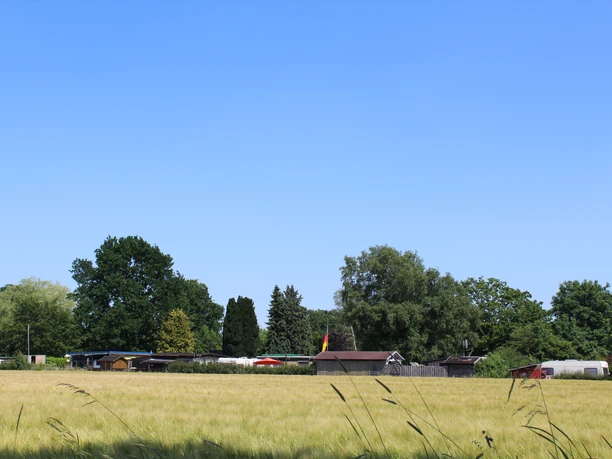 Campingplatz am See Ein Campingplatz am See, von Bäumen und Wiesen umgeben, unter einem strahlend blauen Himmel.