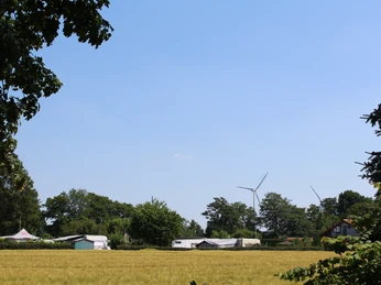 Campingplatz am Ufer eines Sees, umgeben von grünen Bäumen mit Windrädern im Hintergrund.Campsite on the shore of a lake, surrounded by green trees with wind turbines in the background.Campingplads ved bredden af en sø, omgivet af grønne træer med vindmøller i baggrunden.Camping aan de oever van een meer, omgeven door groene bomen met windmolens op de achtergrond.
