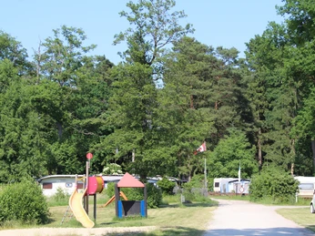 Playground with slide on a campsite, surrounded by caravans and trees under a clear sky.