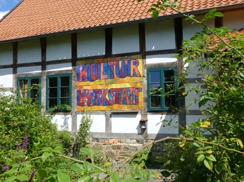 Fachwerkhaus mit zweifarbigen Ziegeln und einem bunten Schild mit der Aufschrift "KulturWerkstatt".