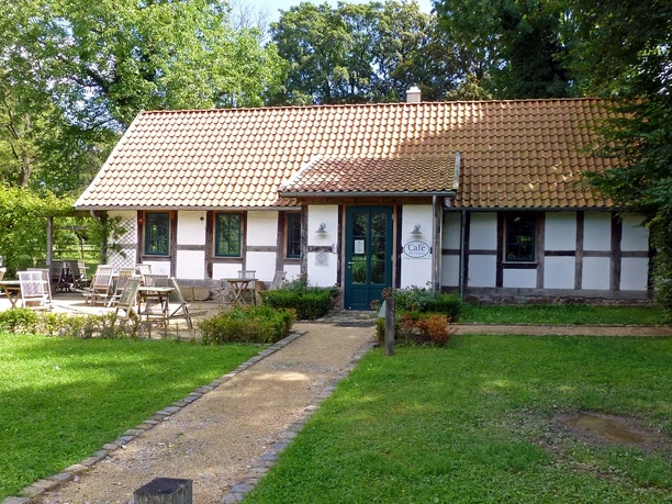 Café Alte Werkstatt Fachwerkhaus mit Café-Schild, Gartenmöbeln auf der Terrasse, umgeben von üppigem Grün.
