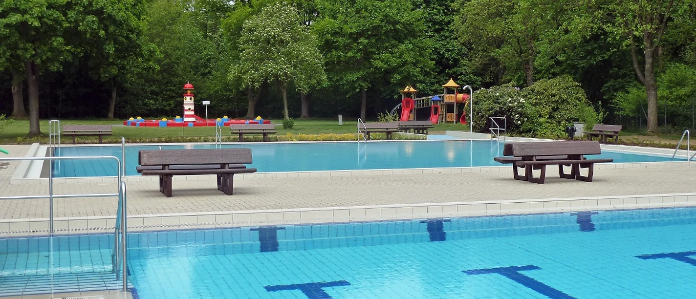 Werburger Waldbad Freibad mit blauem Becken und Sprungturm, umgeben von üppigen Bäumen und bunter Kinderspielanlage.