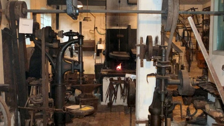Innenansicht einer traditionellen Schmiede mit glühendem Feuer im Ofen, umgeben von Werkzeugen.