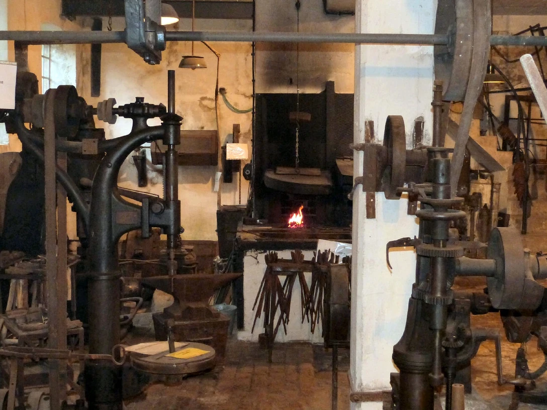 Innenansicht einer traditionellen Schmiede mit glühendem Feuer im Ofen, umgeben von Werkzeugen.