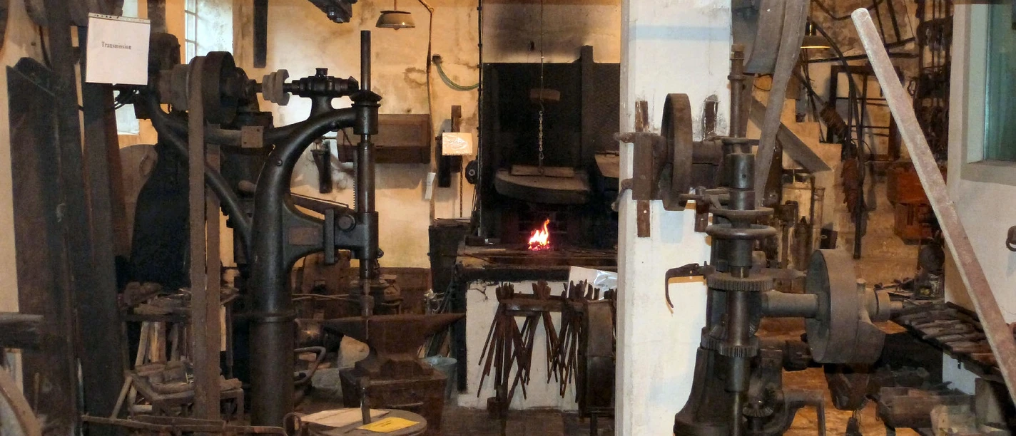 Hammerschmiede Gnuse Innenansicht einer traditionellen Schmiede mit glühendem Feuer im Ofen, umgeben von Werkzeugen.