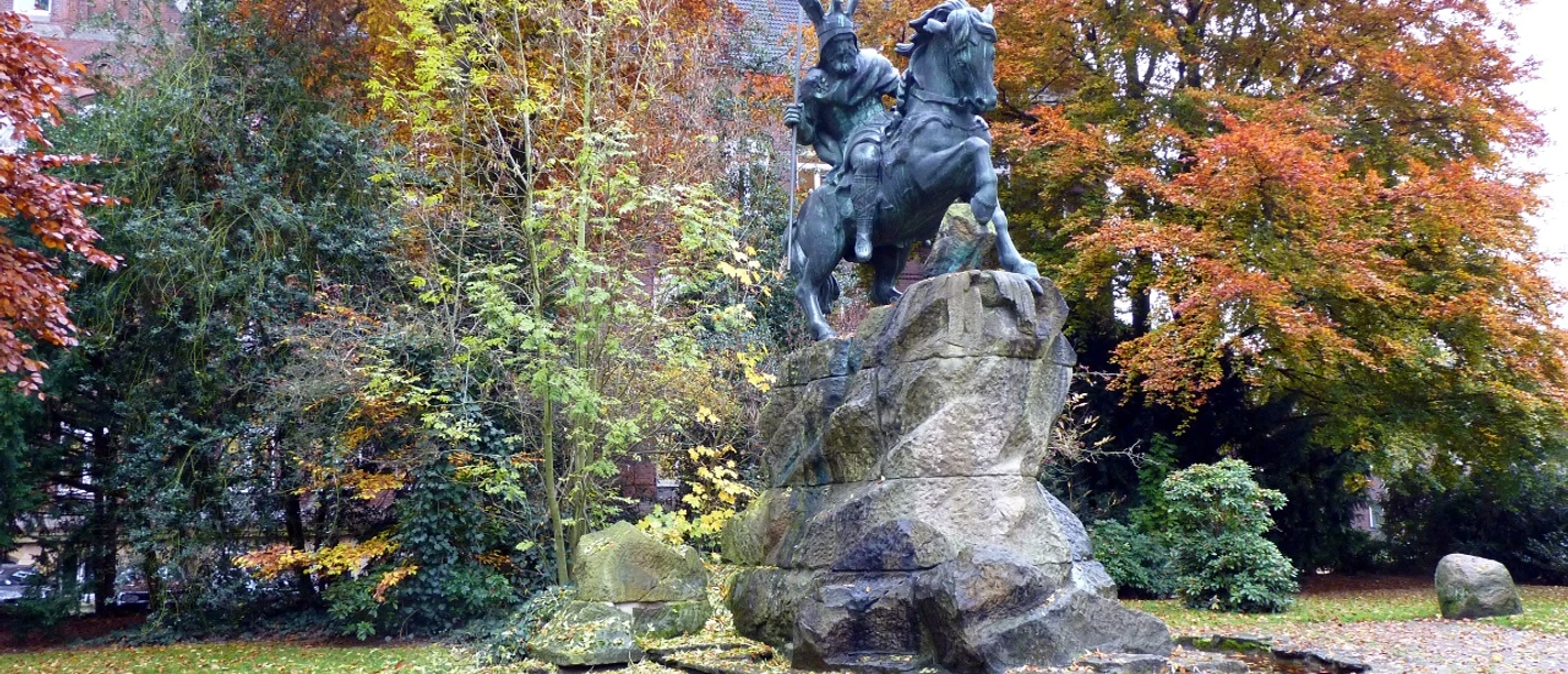 Reiterstandbild von König Wittekind auf einem Felsen, umgeben von buntem Herbstlaub in einem Park.
