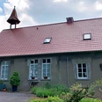Alte Volksschule Rehmerloh Altes Schulgebäude mit rotem Ziegeldach, Glockenturm und gepflegtem Garten, von Bäumen umgeben.